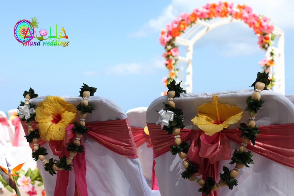 beach wedding with white kukui nut leis with greenery over the white covered chairs on the beach